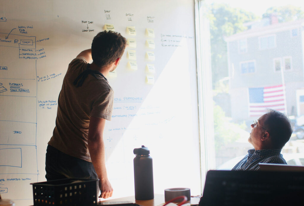 Two colleagues collaborating at a whiteboard covered in sticky notes and diagrams