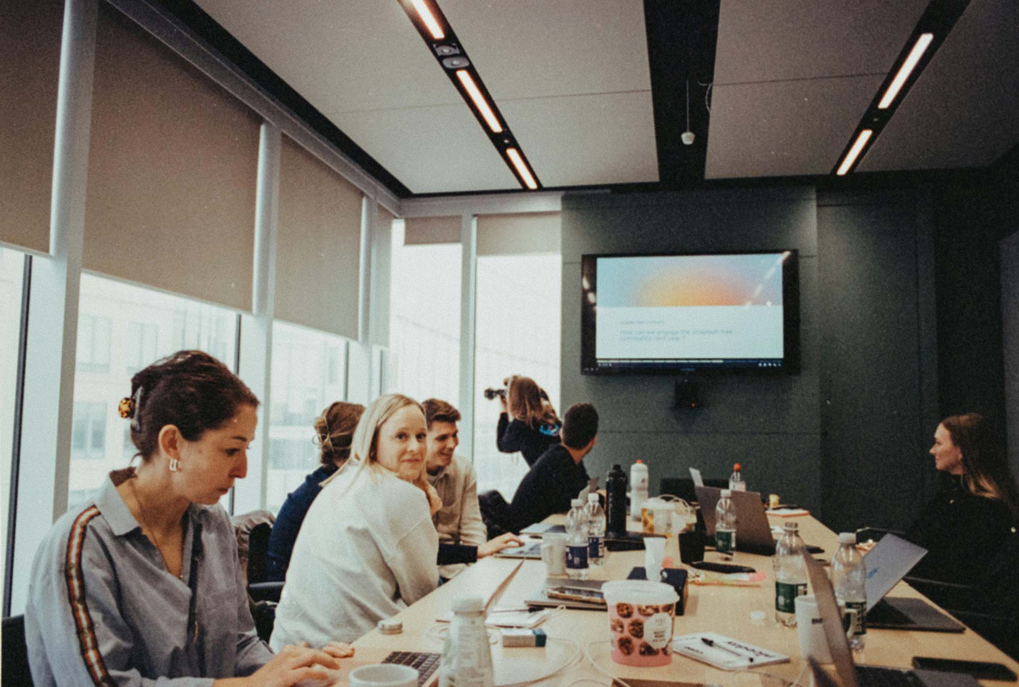 Team seated around a conference table with laptops during a meeting in a bright office with a presentation on the wall screen